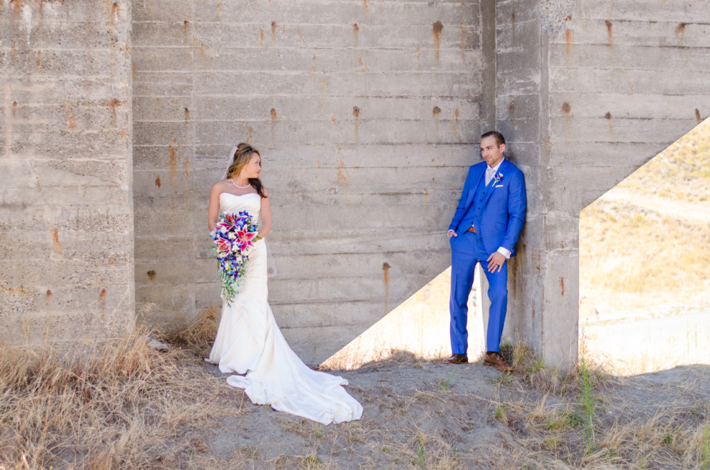 young couple exchanging glances on their wedding day, with bride looking over her shoulder and him leaning on a structure connecting via eye contact