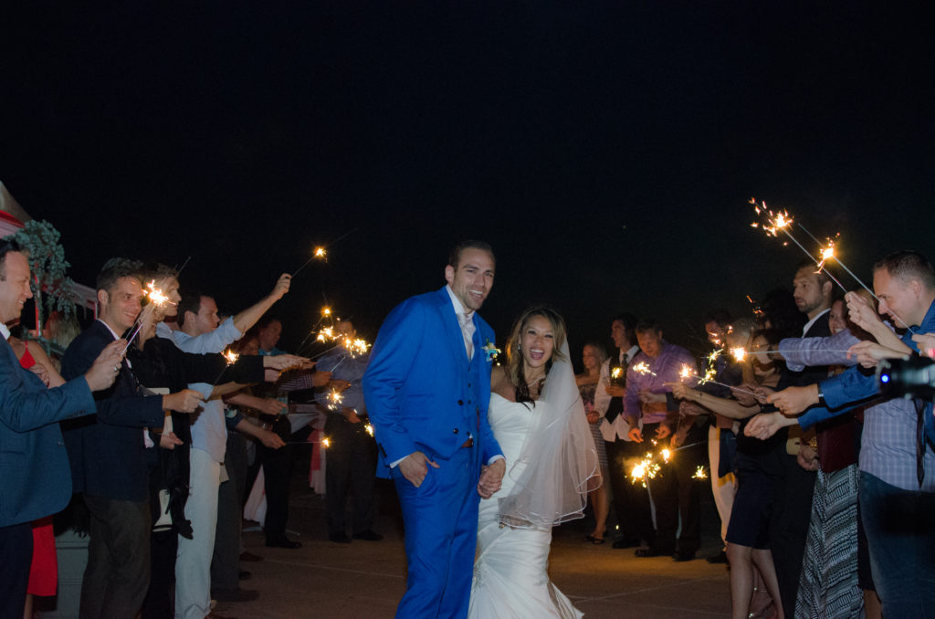 Happy newlywed couple smiling with guests waving sparklers around them at night