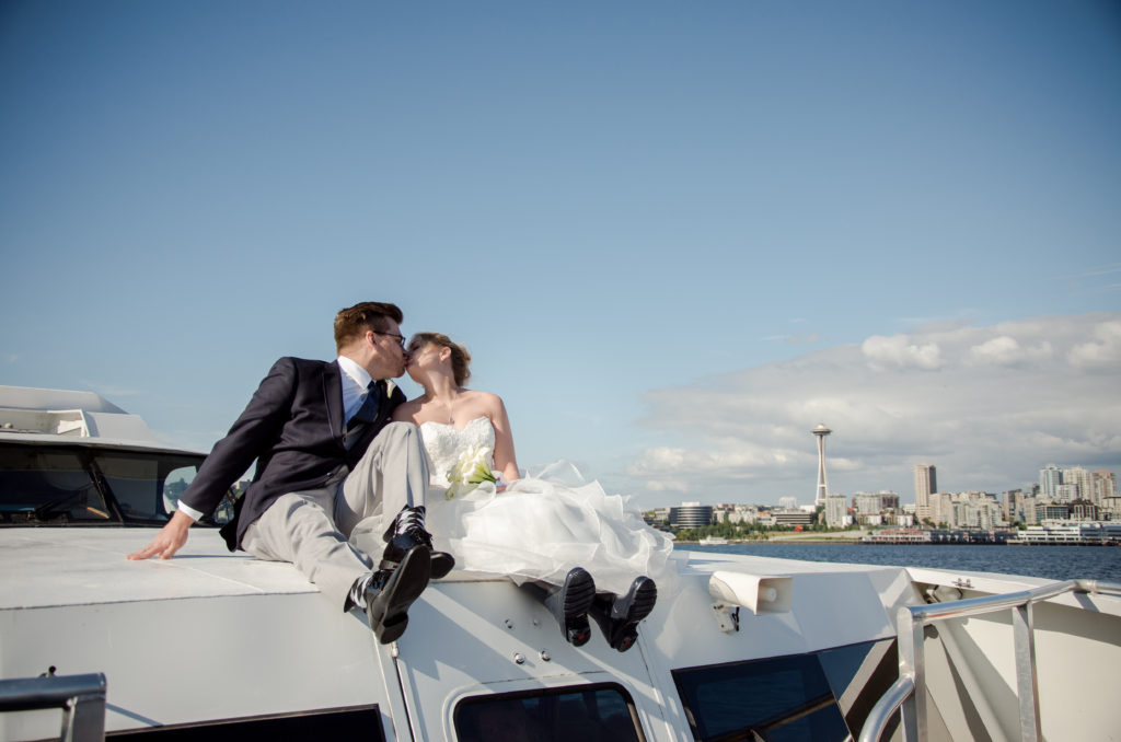 Bride and groom sitting on top of boat with Seattle Skyline in background