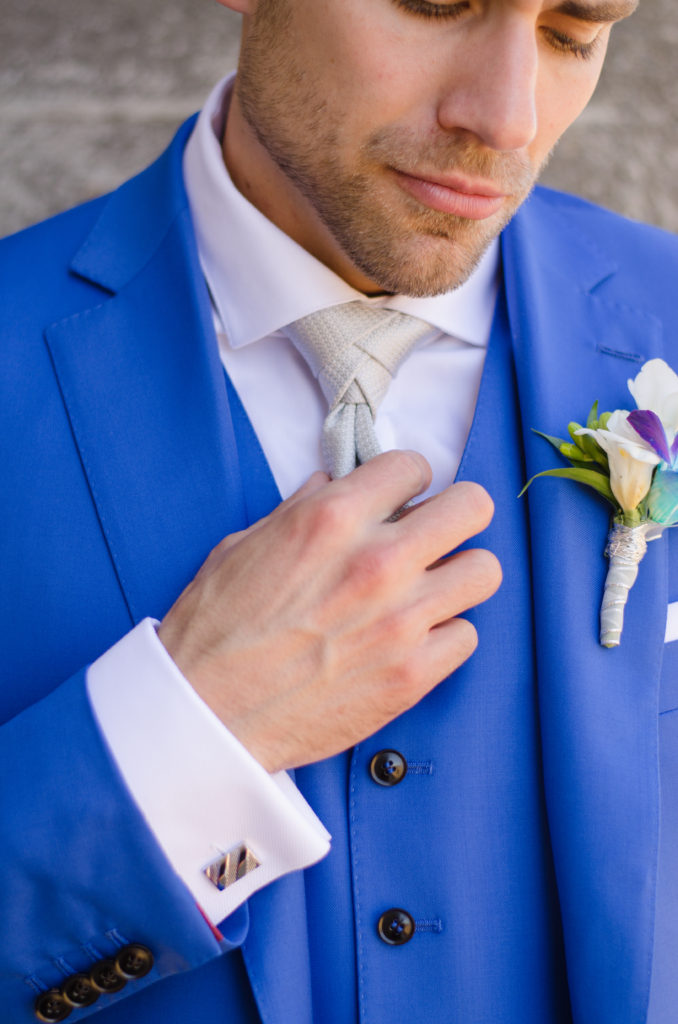 Groom in blue suit adjusting silver tie while looking downward