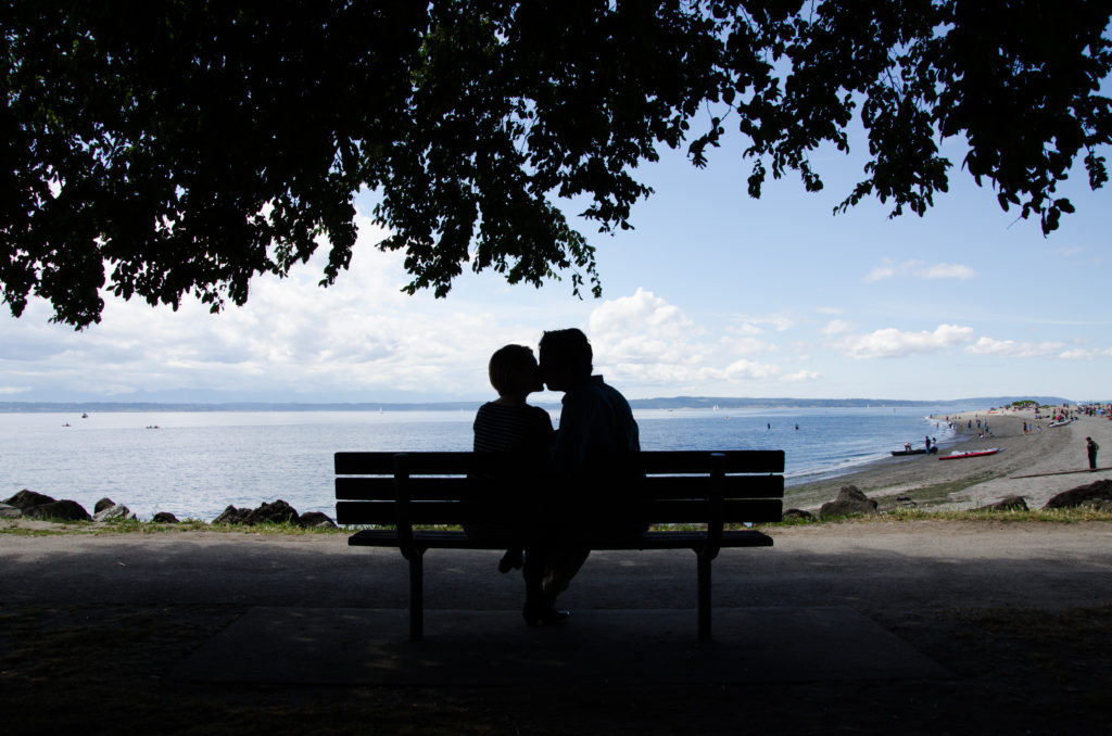 Silhouette of couple kissing on bench near the beach 